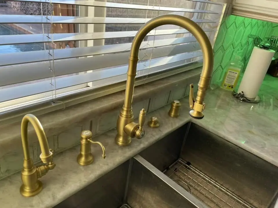 Brushed brass kitchen faucet with a side spray, soap pump and hot-water tap on a marble counter