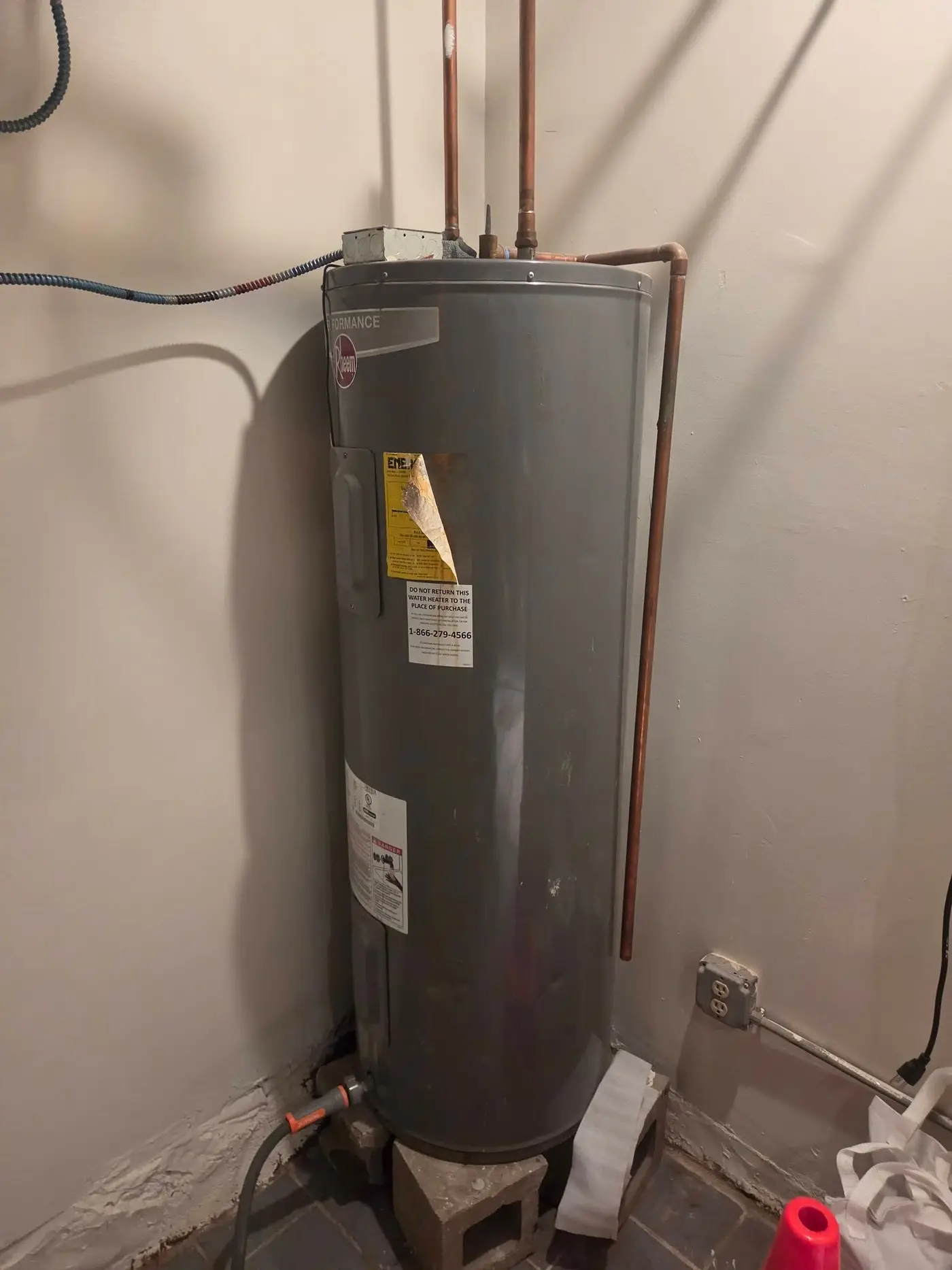 Electric hot water tank installed in a basement corner on concrete blocks with copper supply lines above