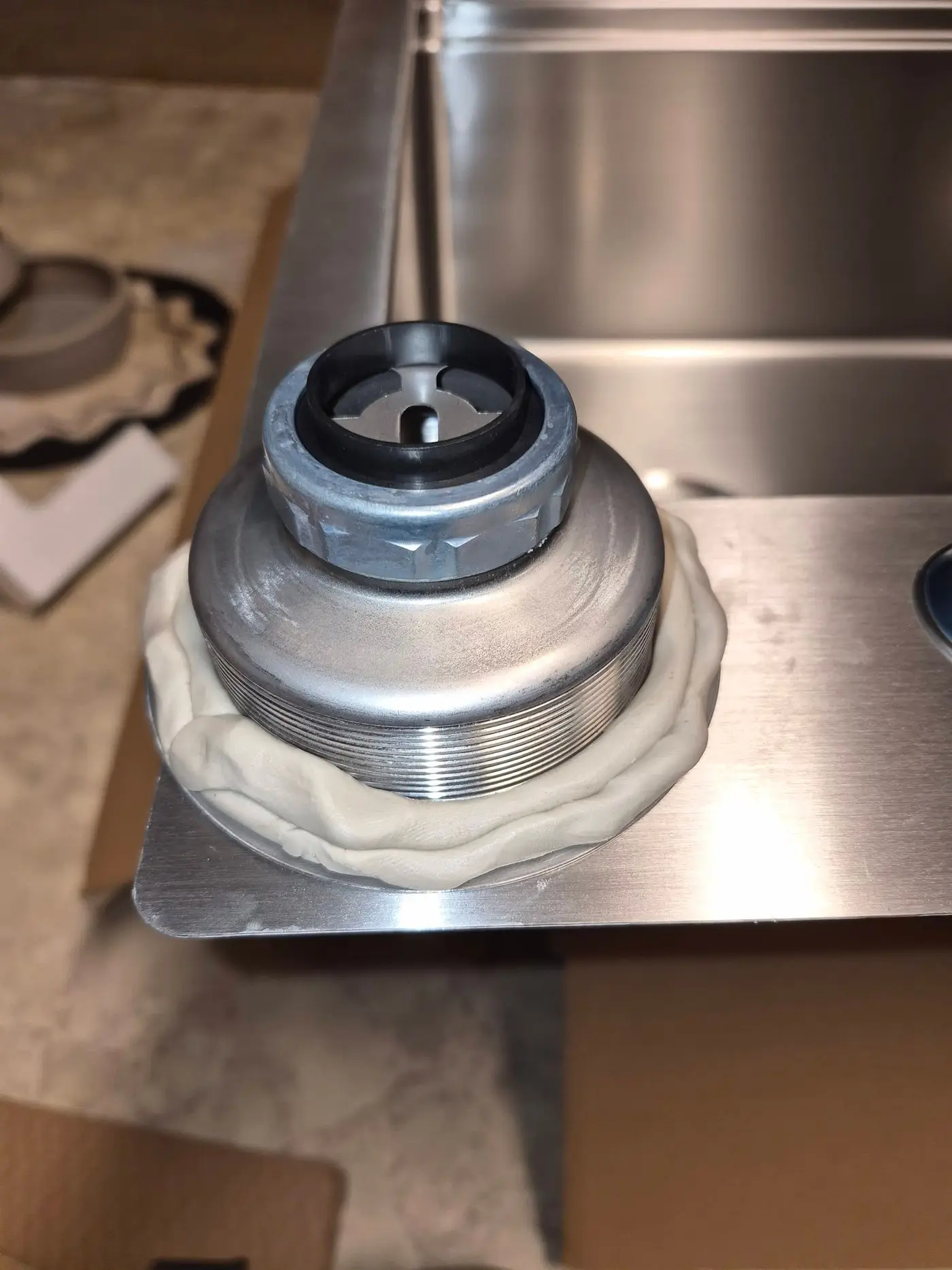 New stainless sink basket strainer seated on a ring of plumber's putty in a kitchen sink drain opening